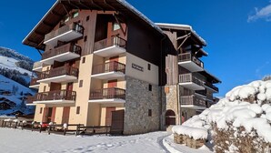 A multi-story hotel with balconies, a stone facade, and a ski slope in the background. - Modern 1-bedroom apartment with pool, near skiing and village (Arêches-Beaufort)