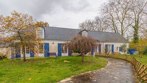 Un chemin de pierres mène à un bâtiment aux volets bleus, et un banc se trouve dans la cour.
