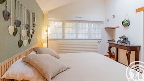 Une chambre à coucher avec un lit, une décoration murale en macramé suspendue, une fenêtre et une table avec une horloge.