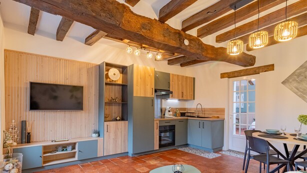 Une cuisine moderne avec des poutres en bois, un téléviseur à écran plat et un coin repas comprenant une table et des chaises.