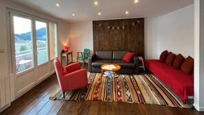 A modern living room with a sofa, armchair, and coffee table, wooden flooring, and a large window with a view. - Charming 2-room apartment in Villard de Lans center (Villard-de-Lans)