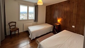 A bedroom with two single beds, a wooden wall, a window with a view, a chair, and a bedside lamp. - Charming 2-room apartment in Villard de Lans center (Villard-de-Lans)