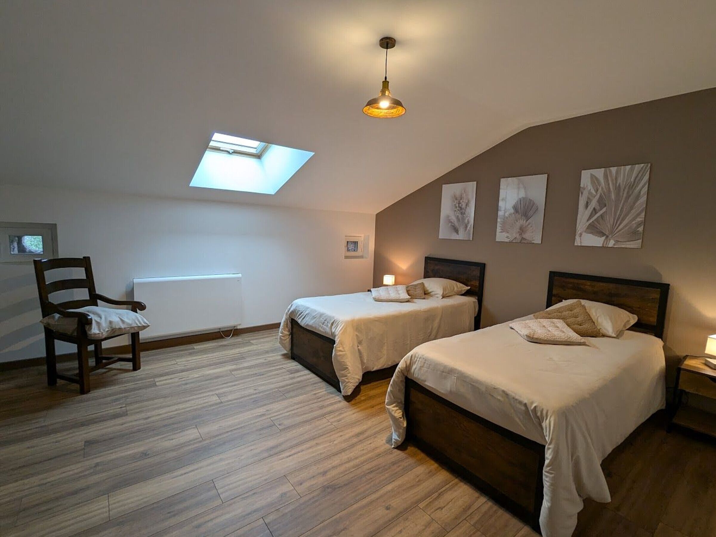 Une chambre avec deux lits, un puits de lumière, un plancher en bois et une chaise.