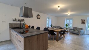 Une cuisine moderne dotée d’un îlot central, un coin repas avec une table en bois et un espace de vie comprenant un canapé et une plante.