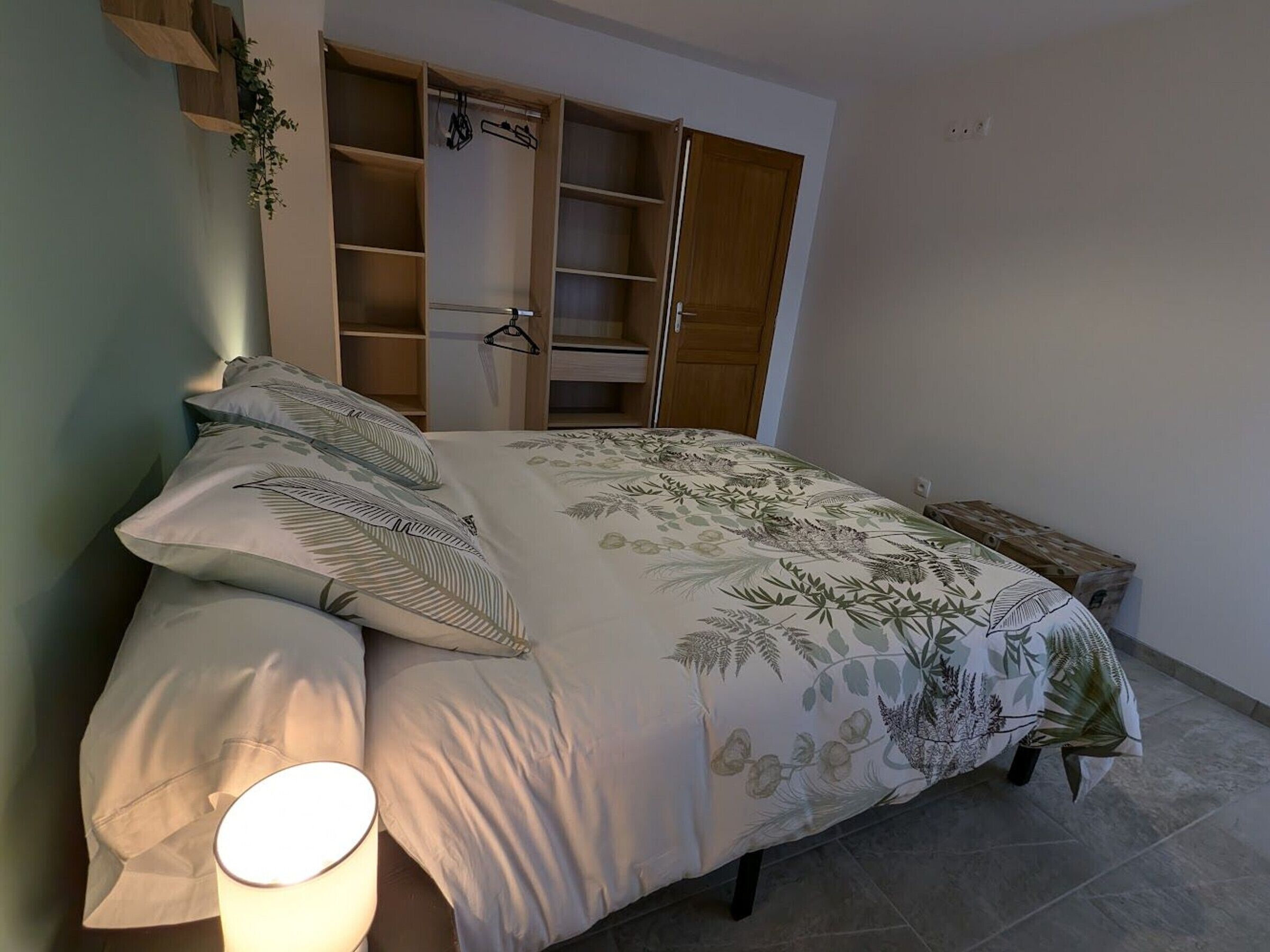 Un dormitorio con cama, lámpara de noche, armario y una mesita con planta.