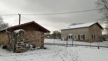 Ein rustikales Steinhaus mit rotem Dach und im Hintergrund ein größeres Gebäude mit beiger Fassade.