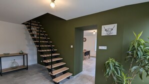 Un escalier avec des marches en bois et des rampes noires, un coin repas avec une table et des chaises, et une plante en pot.