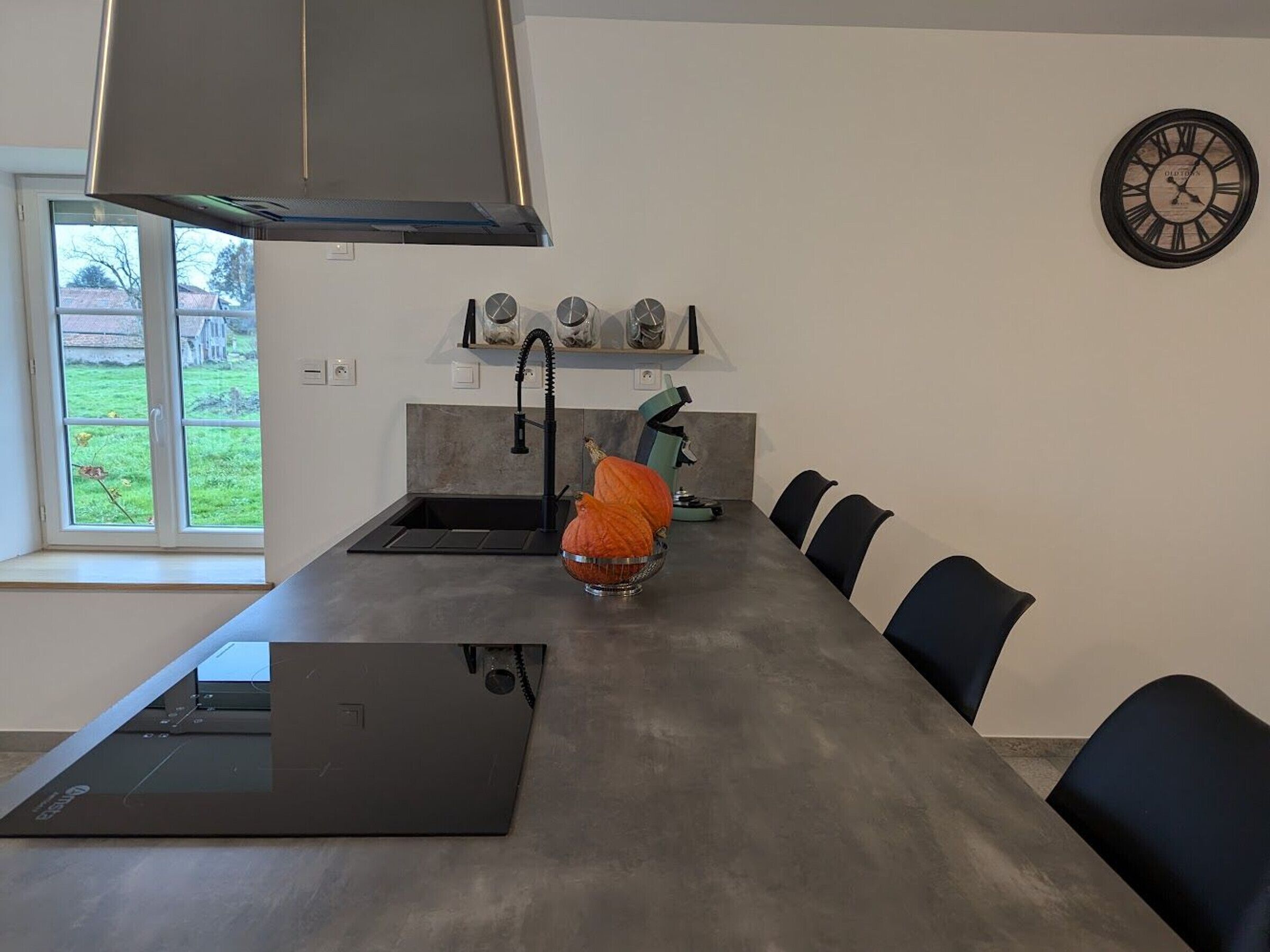 A modern kitchen with a built-in oven, a sink, and a dining area with chairs.