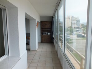 A narrow corridor with a tiled floor, a wooden cabinet with a microwave, and a view of a parking lot through a large window.