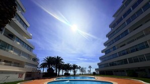 A modern building with a swimming pool, surrounded by palm trees and a clear sky. - Beautiful 3-room apartment in Roses with pool and garden, beach access (Roses)