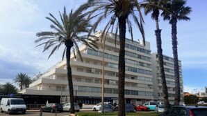 A multi-story hotel with a modern design, featuring a central courtyard with palm trees and a parking area in front. - Beautiful 3-room apartment in Roses with pool and garden, beach access (Roses)