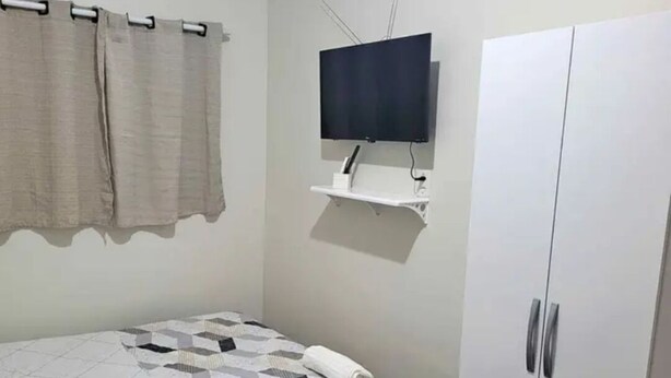 A bedroom with a bed, a TV mounted on the wall, a wardrobe, and a curtain rod. - Hotel Toronto  (Paragominas)