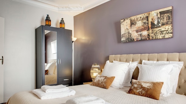 A neatly made bed with white linens and two brown pillows, a dark wardrobe with a mirror, and a wall with a Paris-themed artwork. - Beauregard Design Résidence (Paris)