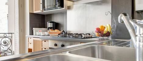 A modern kitchen with stainless steel appliances, a coffee maker, and a fruit basket on the counter.
