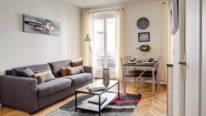 A living room with a grey sofa, a coffee table, and a dining area with a table and chairs. - Beauregard Design Résidence (Paris)