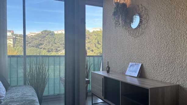 Un balcon donnant sur un paysage verdoyant, un banc en bois et un luminaire fixé au mur.