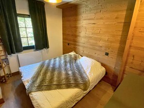 Una habitación con cama, ventana con cortinas, pared de madera y radiador.