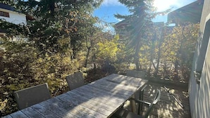 A wooden deck with a table and chairs, surrounded by trees and a building. - Renovated apartment 4 pers, parking, Les Gets (Les Gets)