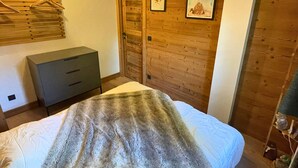 A bedroom with a bed, a dresser, wooden panel walls, and a door. - Renovated apartment 4 pers, parking, Les Gets (Les Gets)
