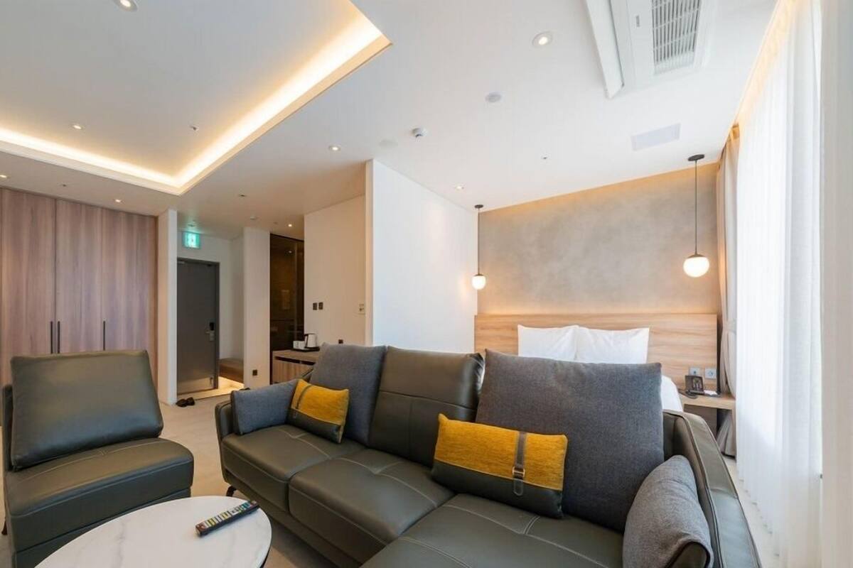 A modern hotel room with a sofa set, a coffee table, and a bed with a wooden headboard.