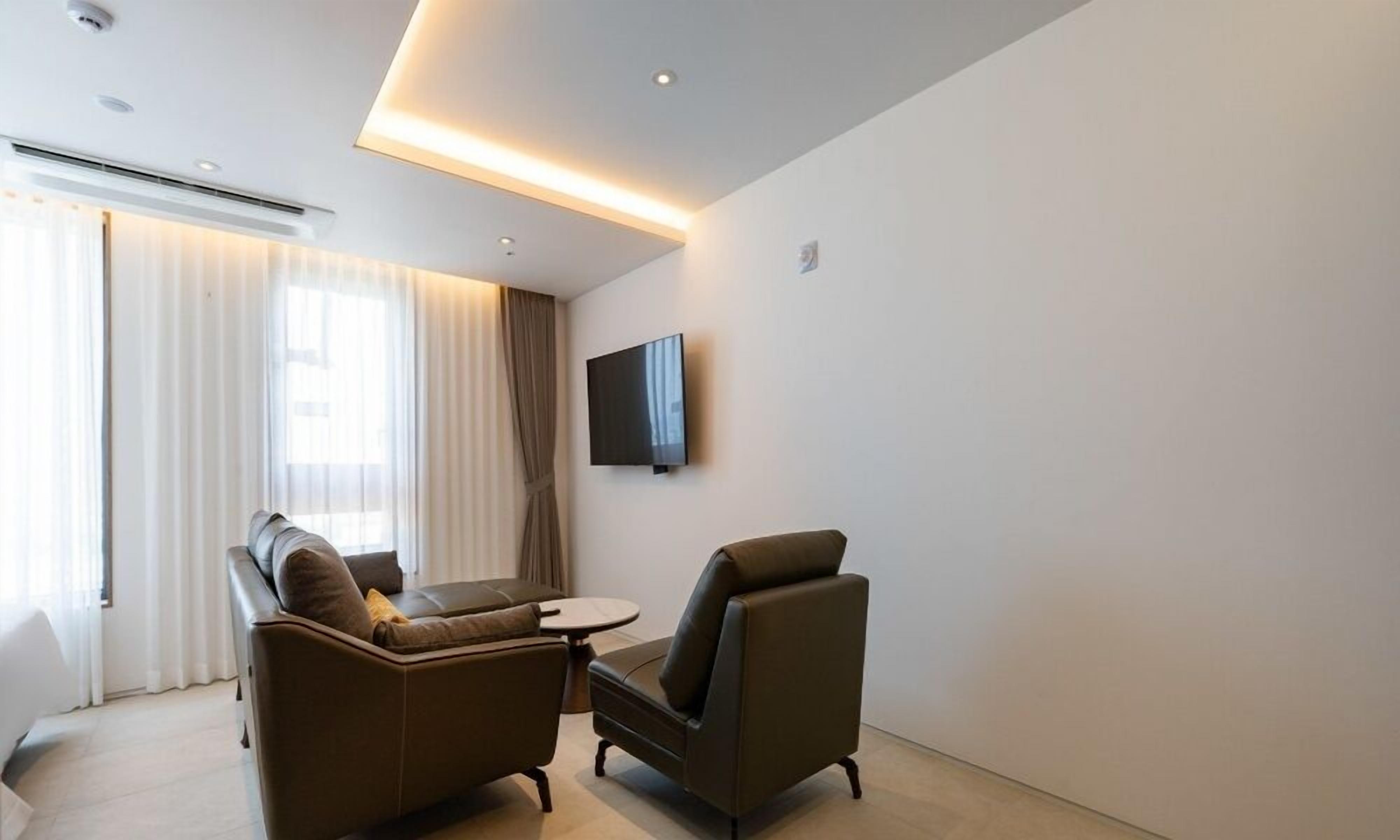 A modern hotel room with a sofa, armchair, and a small table.