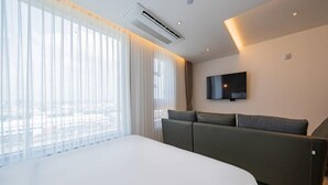 A modern hotel room with a large bed, a flat-screen TV mounted on the wall, and a view of the city through large windows. - THE HOUND HOTEL BANDALISLAND 2 (Ansan)
