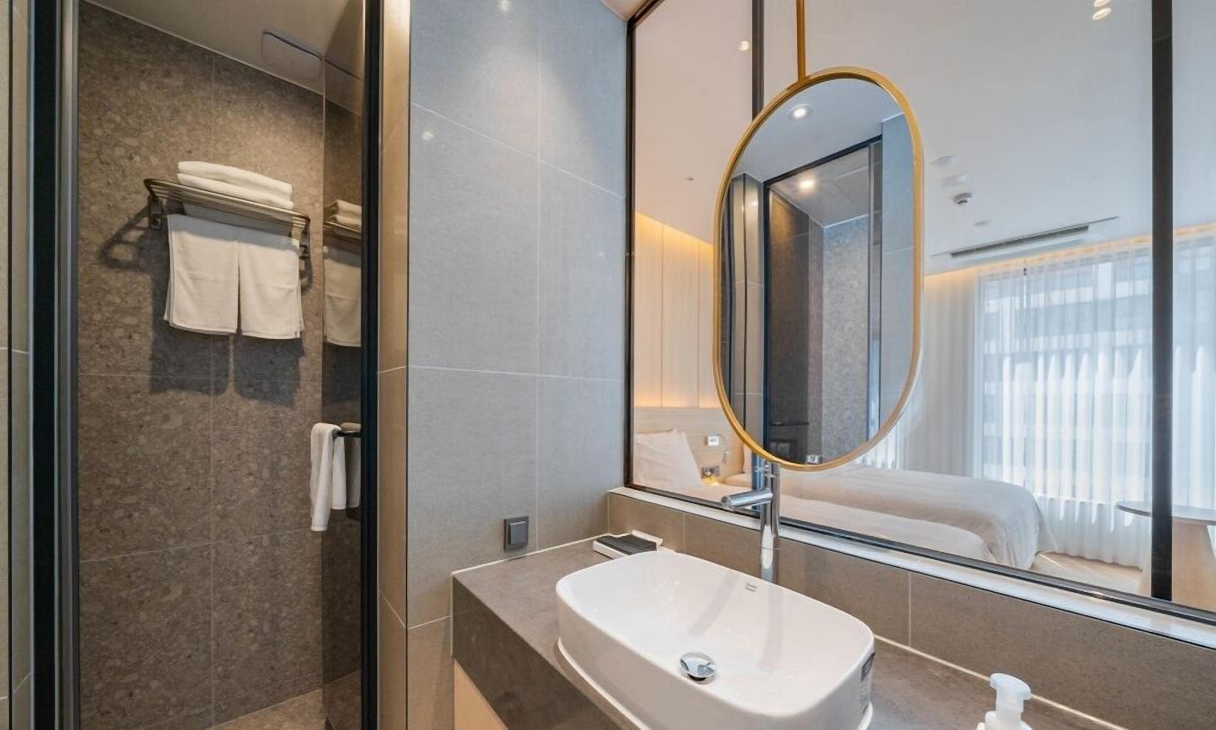 Un baño moderno con un espejo ovalado grande, un lavamanos y una cabina de ducha de vidrio.