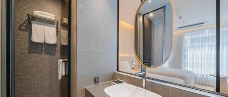 Un baño moderno con un espejo ovalado grande, un lavamanos y una cabina de ducha de vidrio.