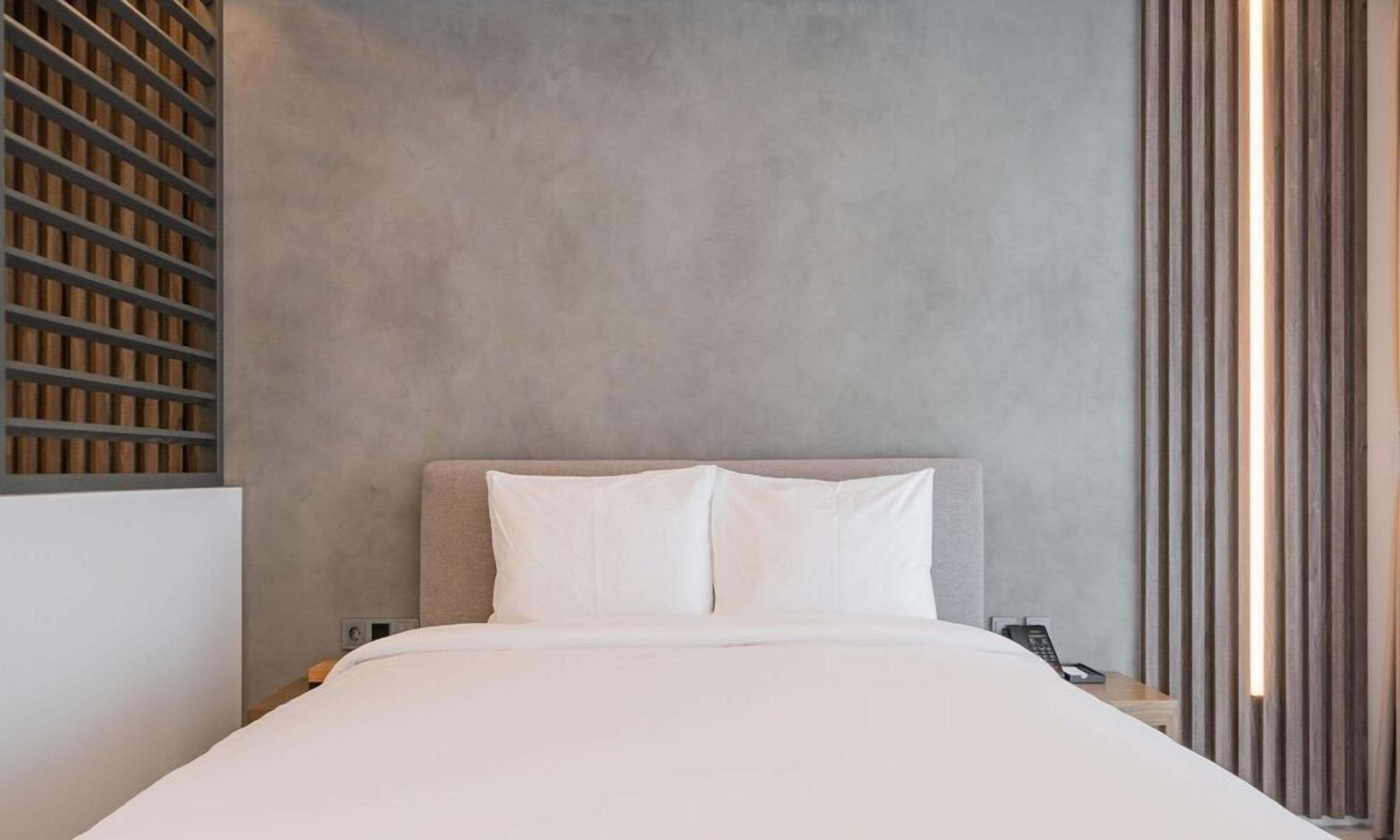 Quarto moderno com cabeceira cinza, roupa de cama branca e painel de parede em ripas de madeira.