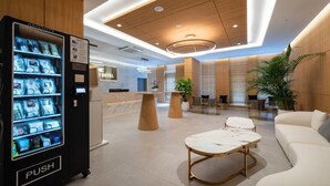 A hotel lobby with a reception desk, a push vending machine, seating area, and a large plant. - THE HOUND HOTEL BANDALISLAND 2 (Ansan)