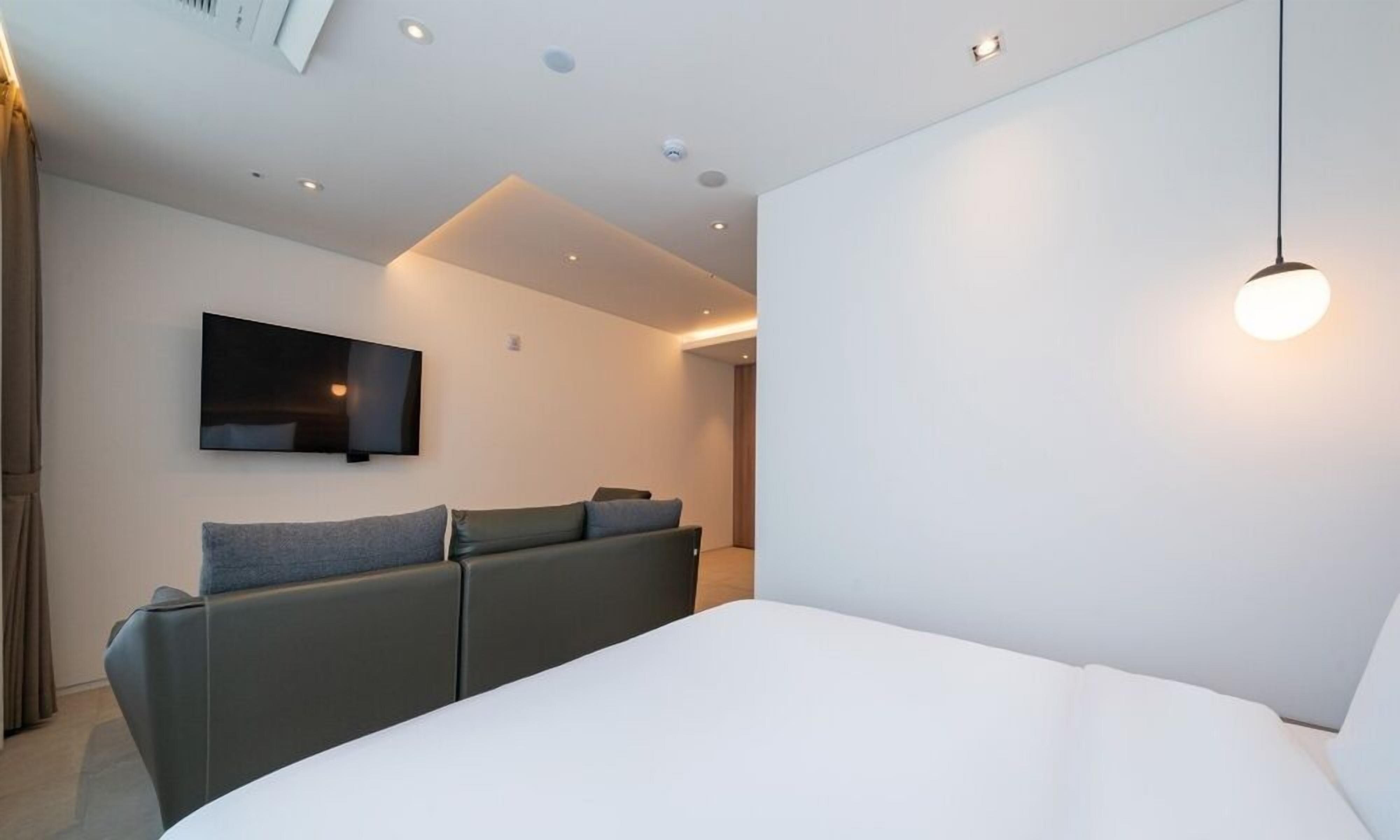 Una habitación de hotel moderna con una cama grande, un sofá, un televisor de pantalla plana montado en la pared e iluminación empotrada en el techo.