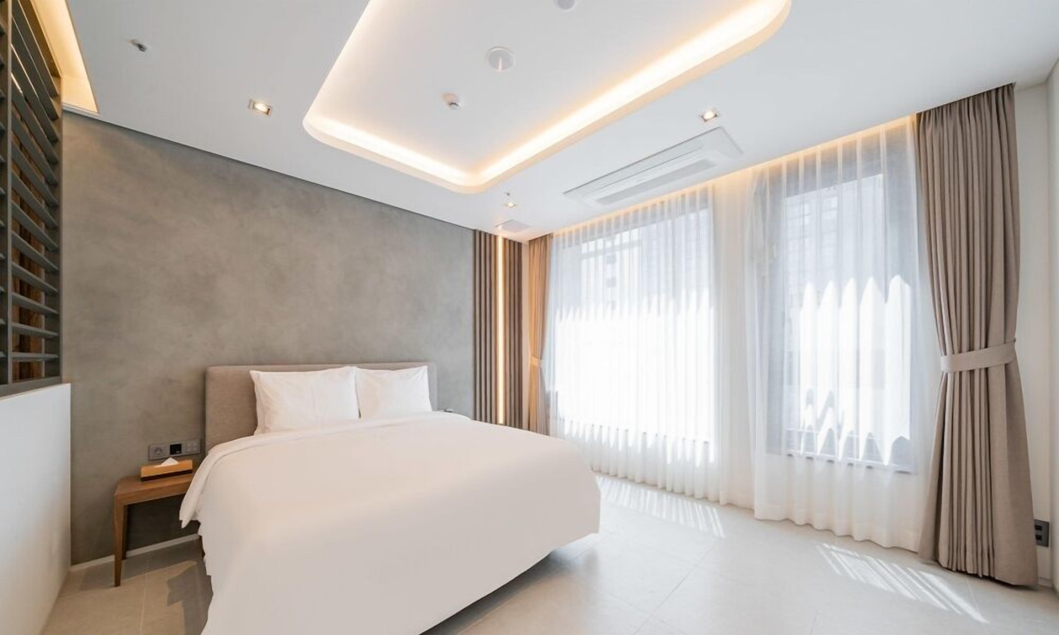 A modern bedroom with a large bed, a bedside table, a built-in shelf, and a large window with curtains.