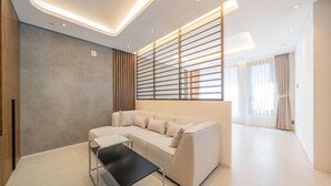 A modern living room with a sectional sofa, a glass coffee table, and a contemporary ceiling design. - THE HOUND HOTEL BANDALISLAND 2 (Ansan)