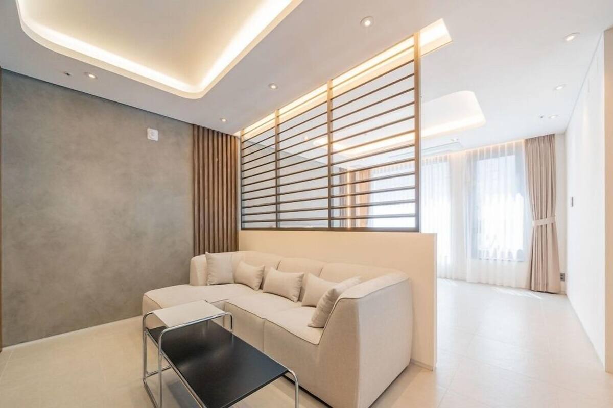 A modern living room with a sectional sofa, a glass coffee table, and a contemporary ceiling design.