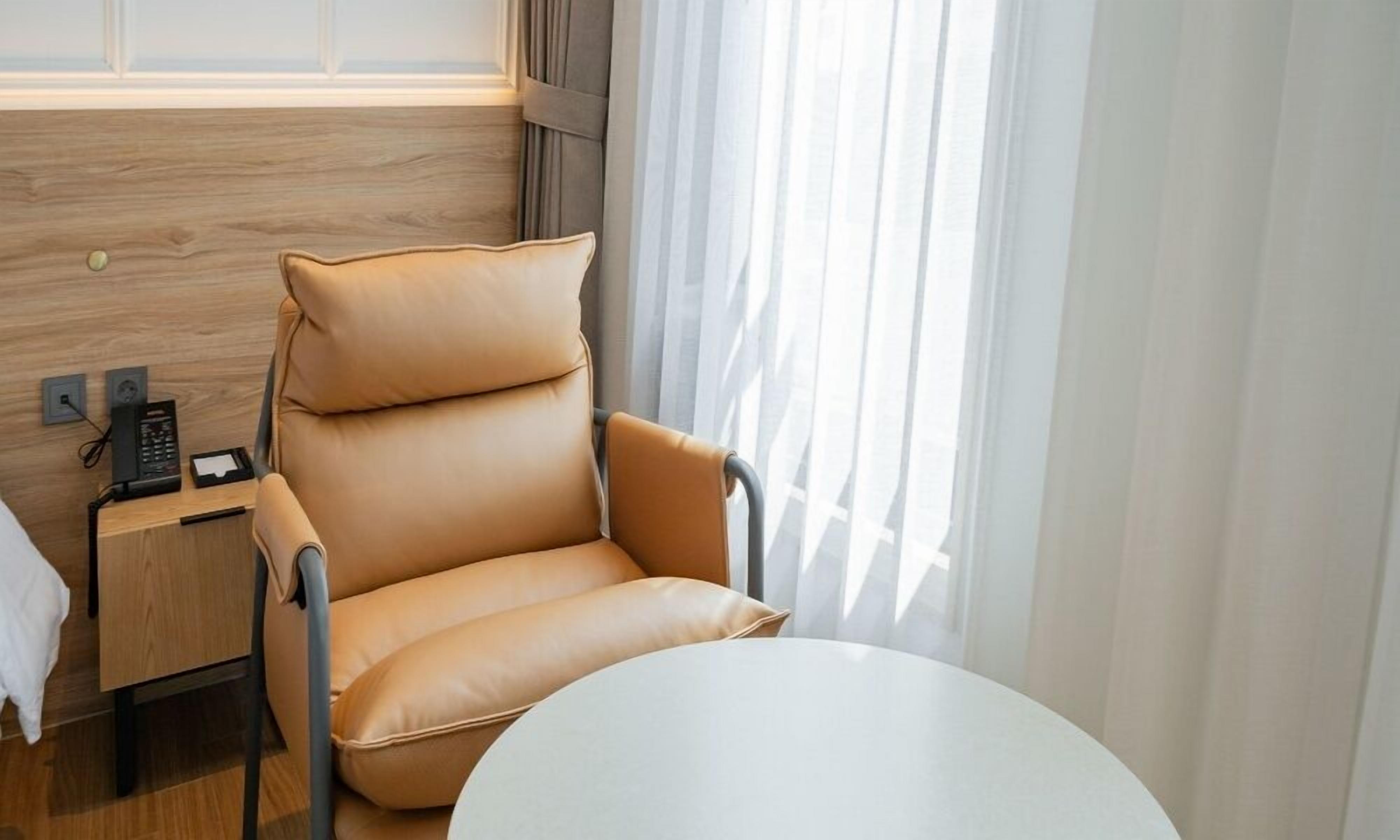 Une chambre d’hôtel moderne, dotée d’un fauteuil en cuir, d’une table de chevet avec un téléphone et un chargeur, et d’une table ronde.