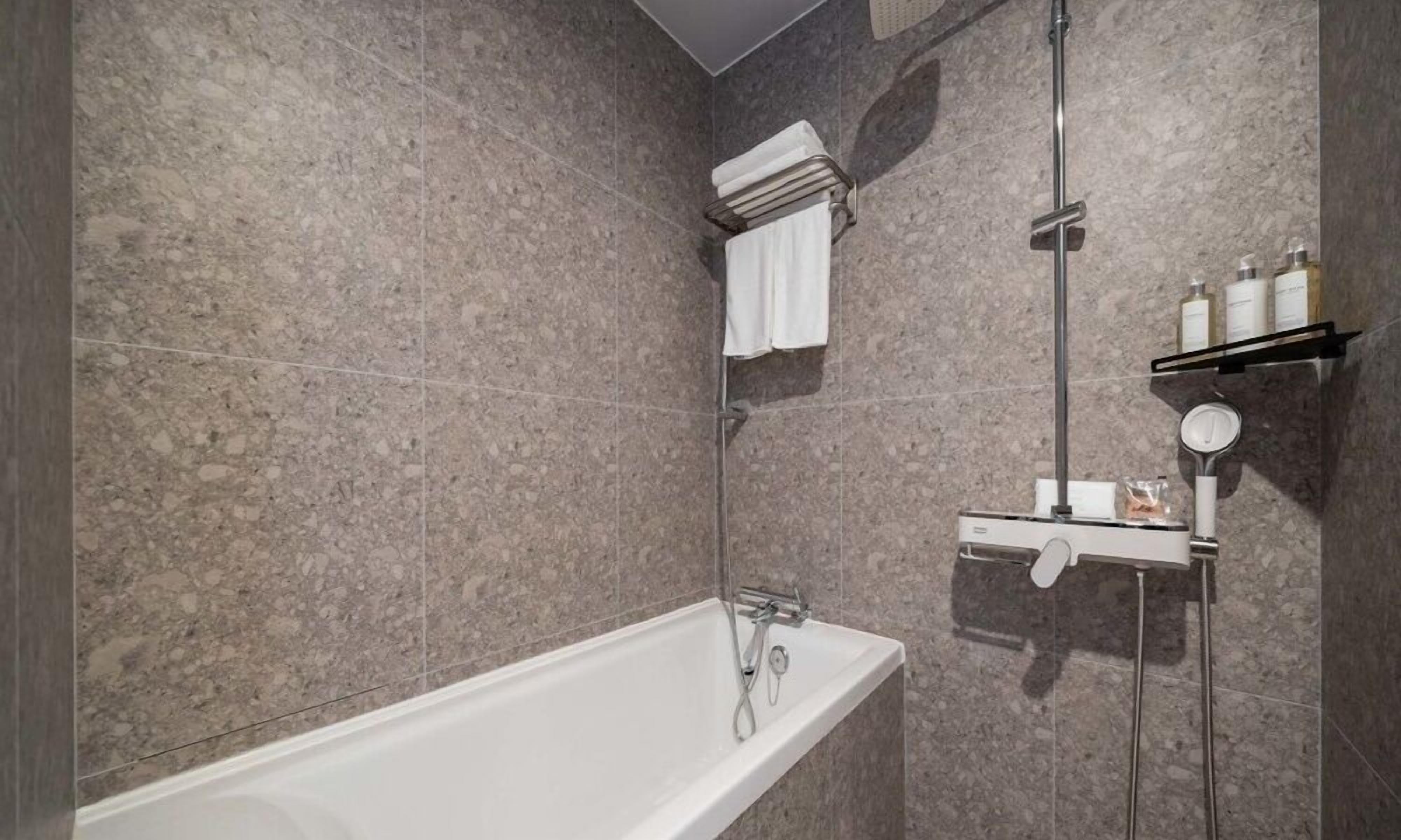 Un baño moderno con una bañera independiente, cabina de ducha con mampara de vidrio y un estante con artículos de aseo.