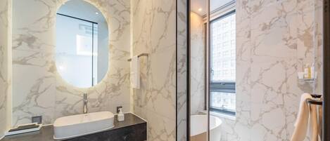 A modern bathroom with marble walls, a large mirror, a sink, and a bathtub.
