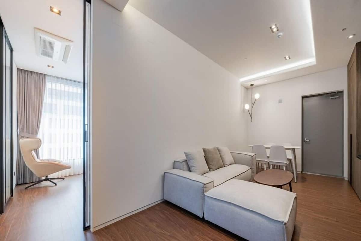 A modern living room with a sofa, a dining table with chairs, and a kitchen area with a refrigerator.