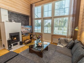 A cozy living room with a fireplace, a sofa, a coffee table, and a large window with blinds.