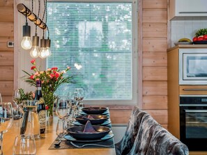 A dining area with a wooden table set for a meal, a window with blinds, and a kitchen area with appliances. - Rukan tunturituuli by Interhome (Kuusamo)