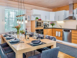 A modern kitchen with white cabinets, stainless steel appliances, and a dining area set for six with a wooden table and grey chairs.