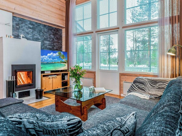 A cozy living room with a fireplace, a television, and a large window with blinds.