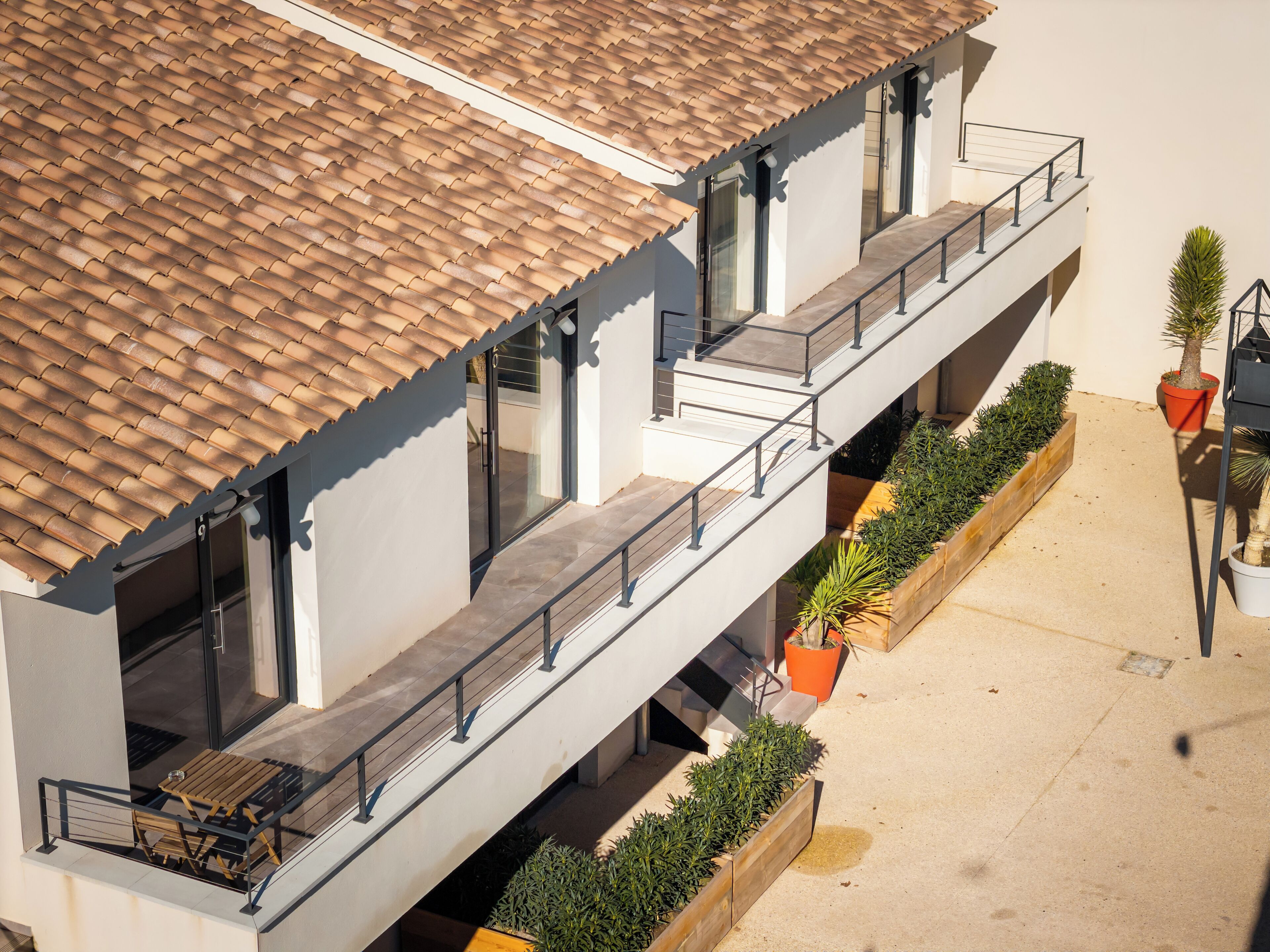 A modern building with a tiled roof, balconies with railings, and potted plants.