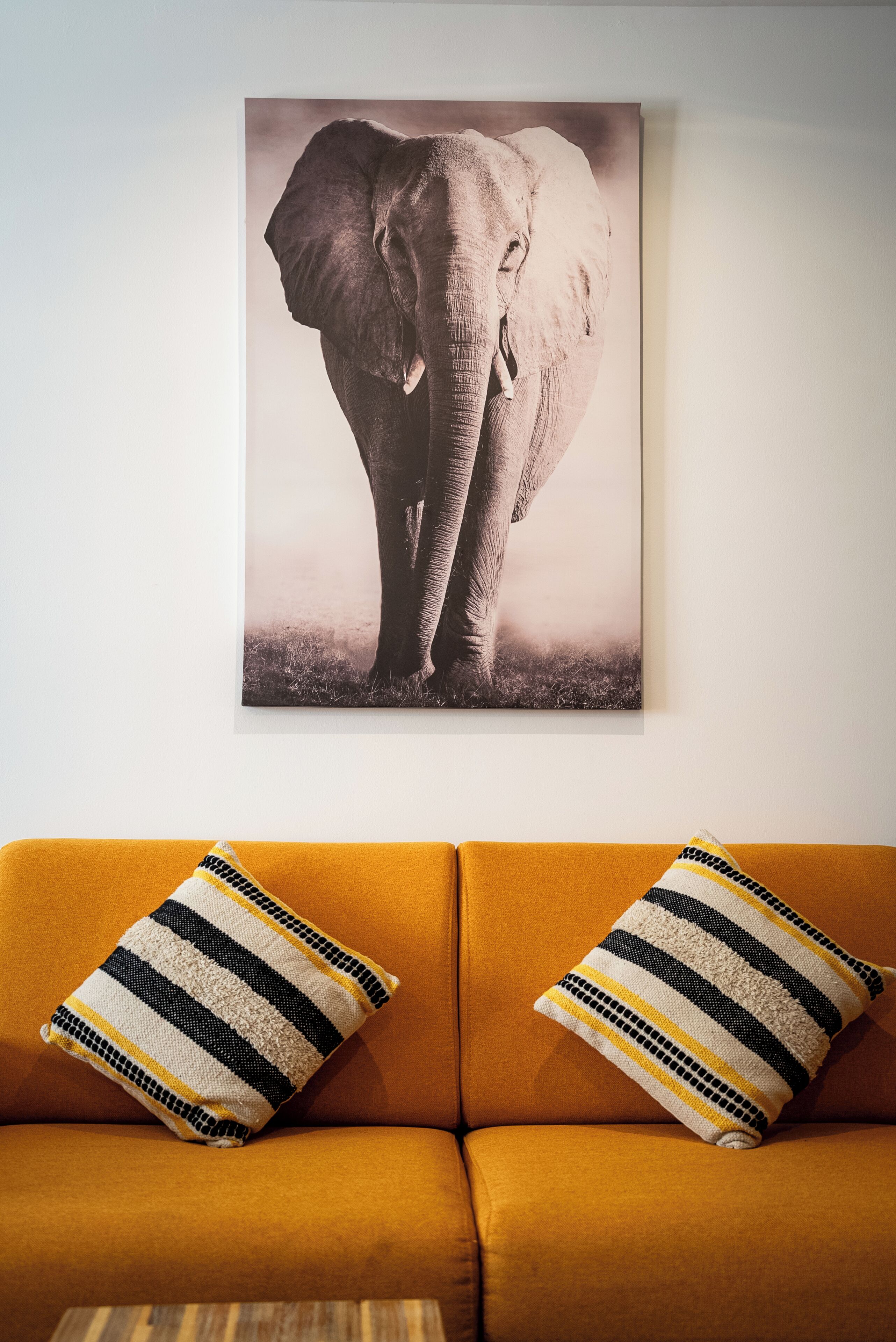Una habitación con un cuadro grande de un elefante en la pared, un sofá color mostaza y almohadones a rayas.