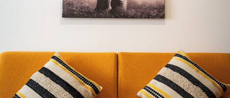 Una habitación con un cuadro grande de un elefante en la pared, un sofá color mostaza y almohadones a rayas.