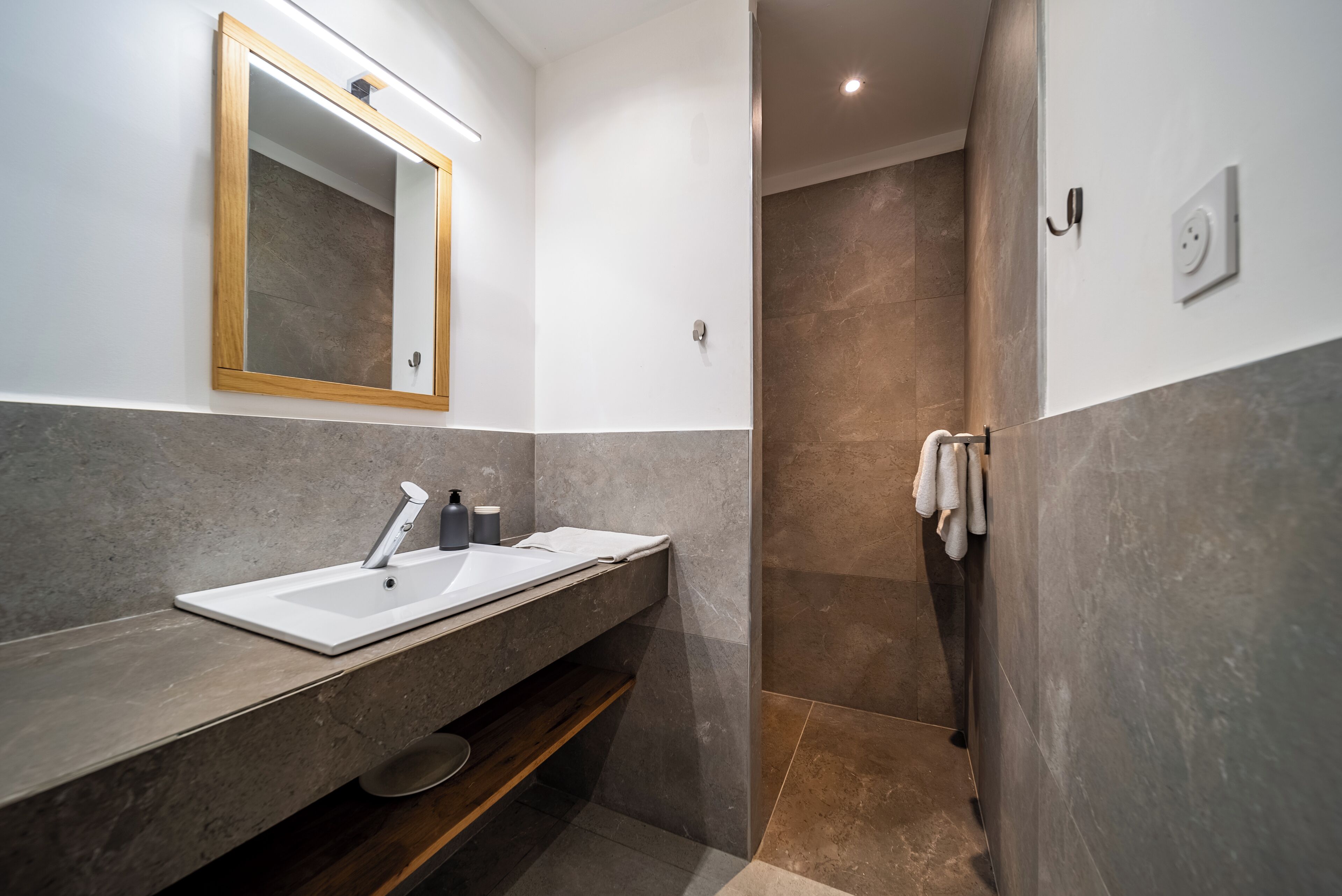 A modern bathroom with a dual sink vanity, a large mirror, and a shower area.