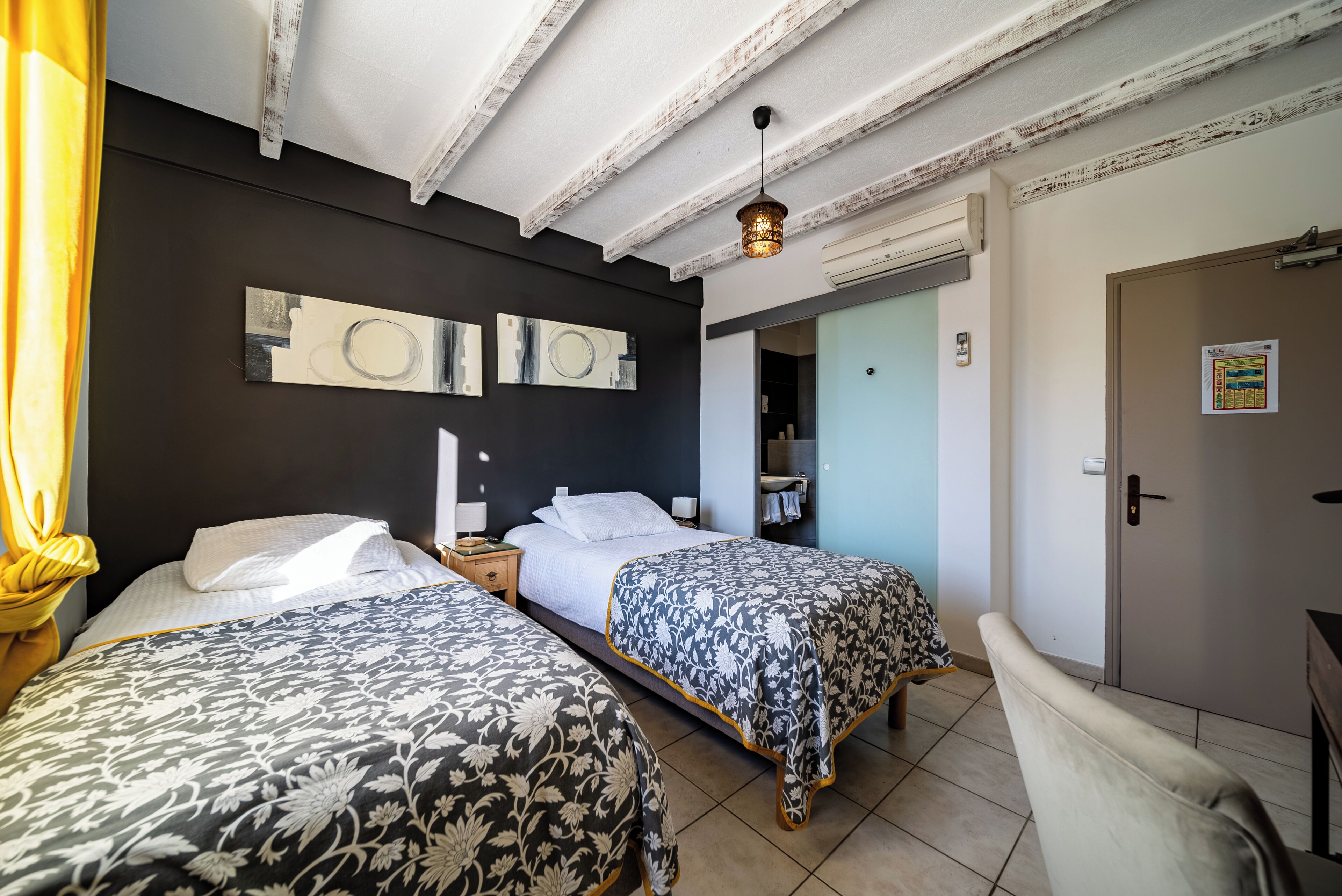Ein Zimmer mit zwei Betten, einem Nachttisch, einer Lampe, einem Deckenventilator und einer Tür.