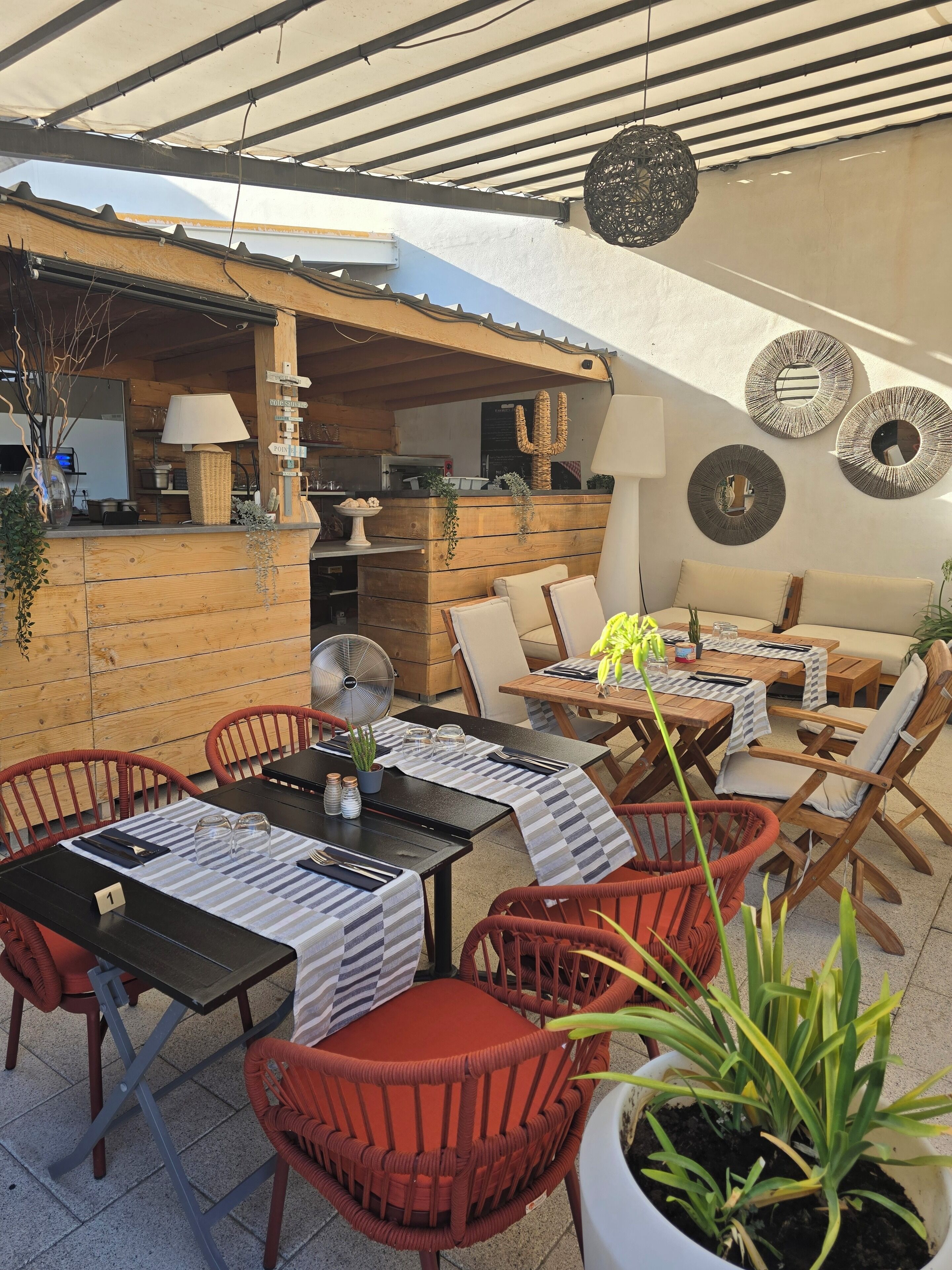 An outdoor patio area with wooden furniture, tables, and chairs. There are decorative wall pieces and a cactus decoration.