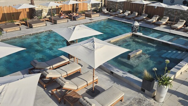 A pool area with multiple lounge chairs and umbrellas, surrounded by stone walls and wooden fences. - Les Loges du Luberon (Cabrieres-d'Avignon)