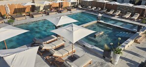Un espace piscine doté de plusieurs chaises longues et de parasols, entouré de murs en pierre et de clôtures en bois.
